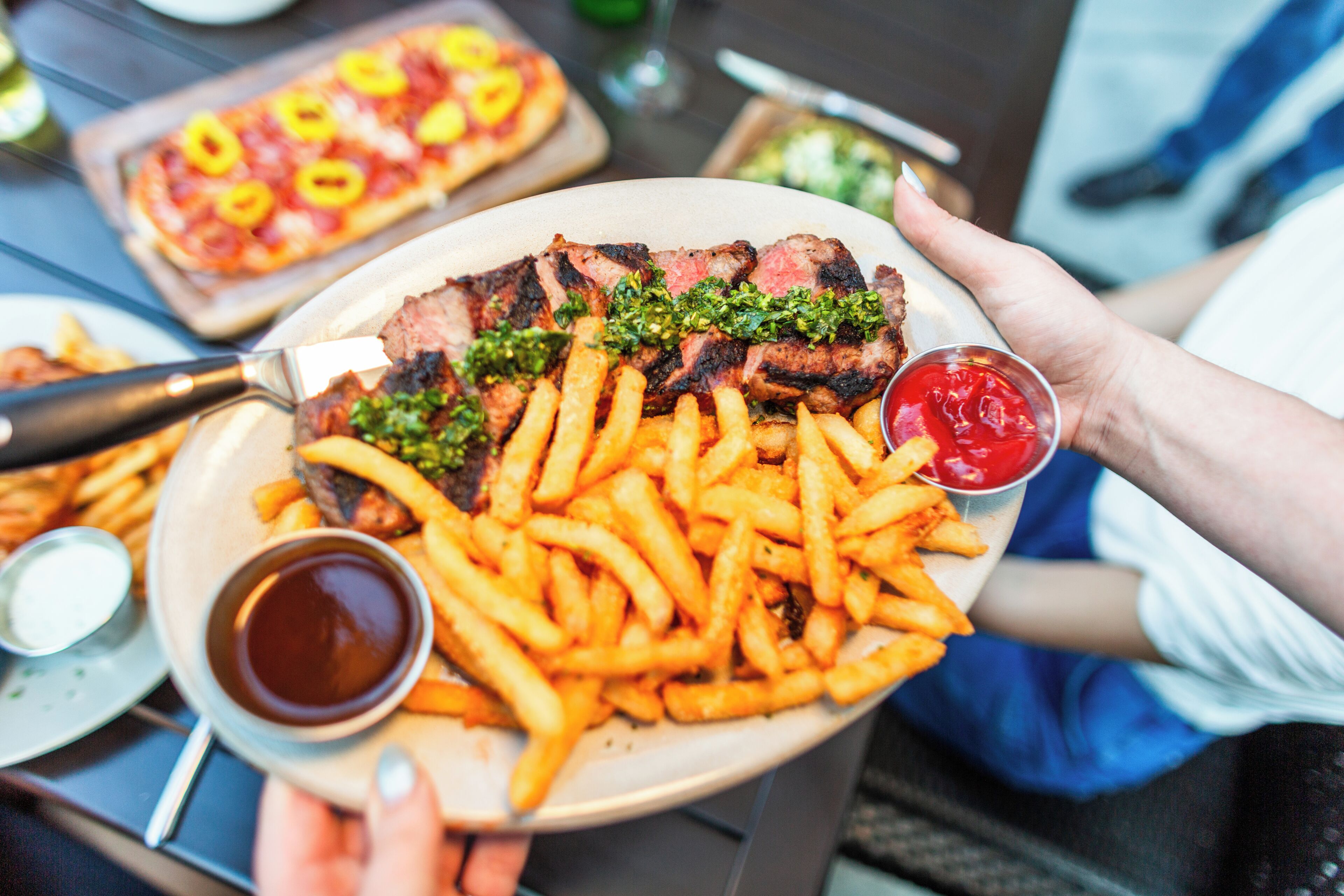 A plate of steak with fries and ketchup, held by a person.