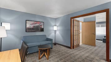 A hotel room with a blue sofa, a small round table, a lamp, and a door leading to another room.