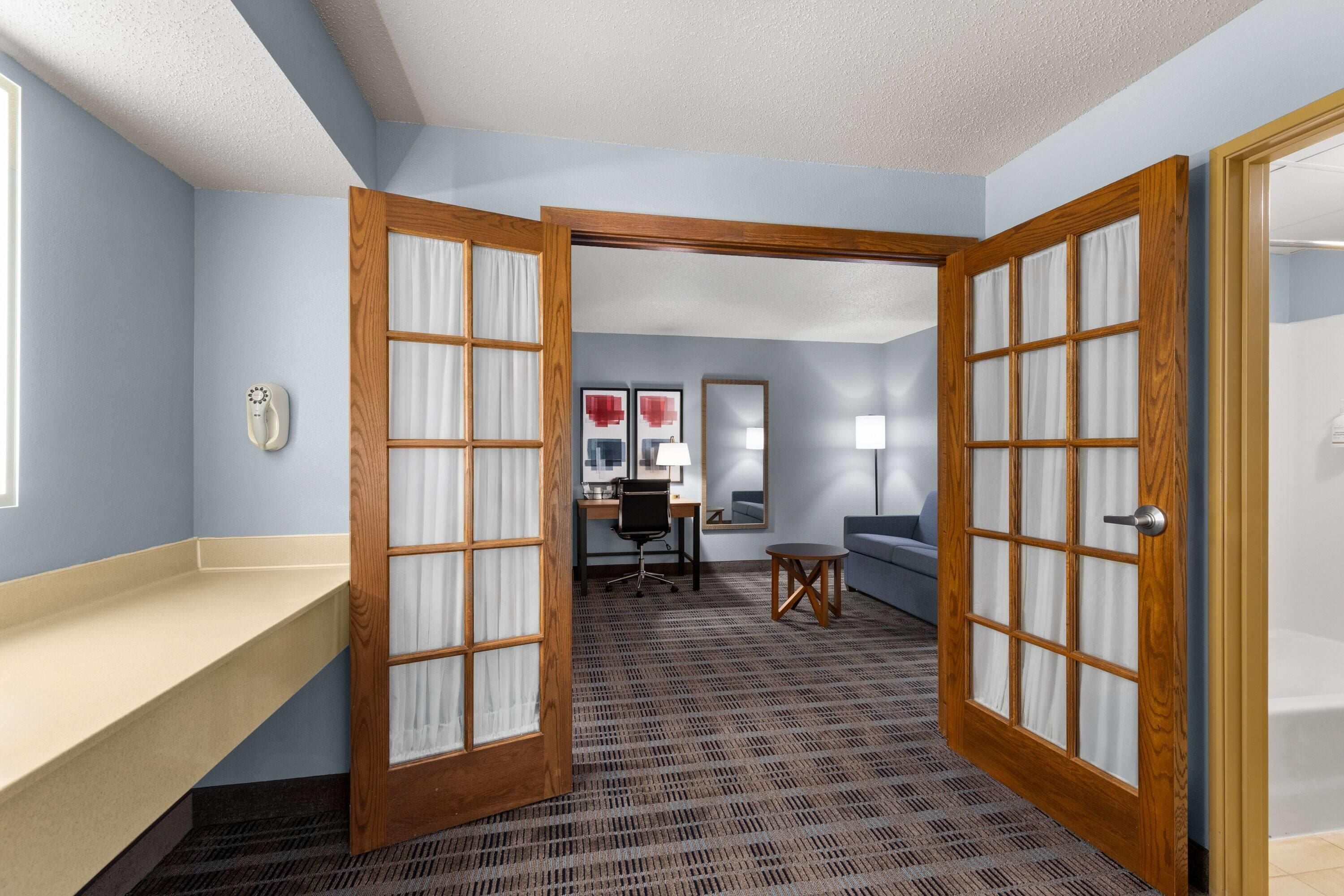 Une chambre d’hôtel avec une salle de bain, un bureau, une chaise, un canapé et un miroir.