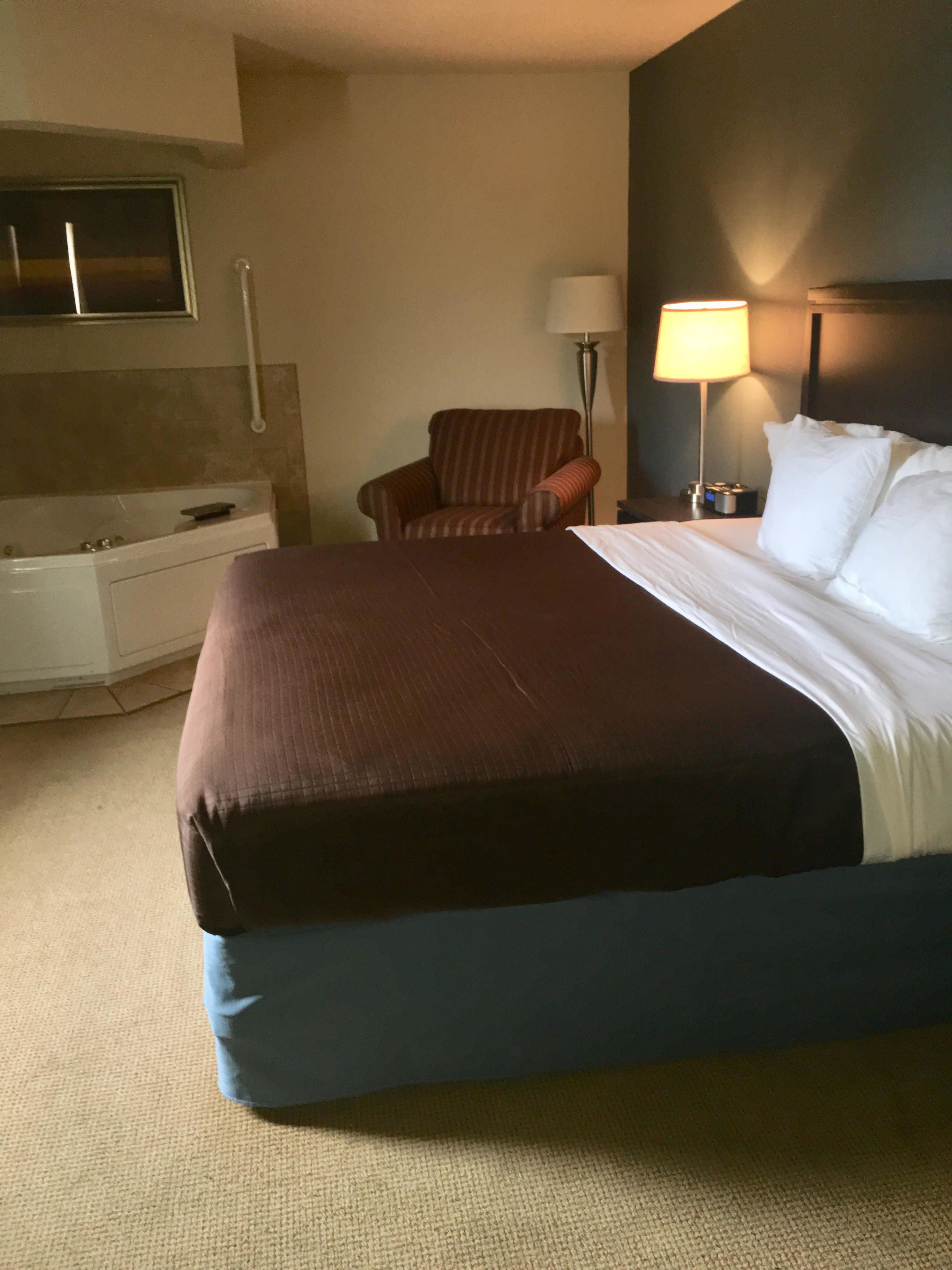 Une chambre d’hôtel avec un grand lit, une chaise, un bureau avec une lampe et un téléviseur fixé au mur.