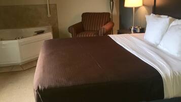Une chambre d’hôtel avec un grand lit, une chaise, un bureau avec une lampe et un téléviseur fixé au mur.