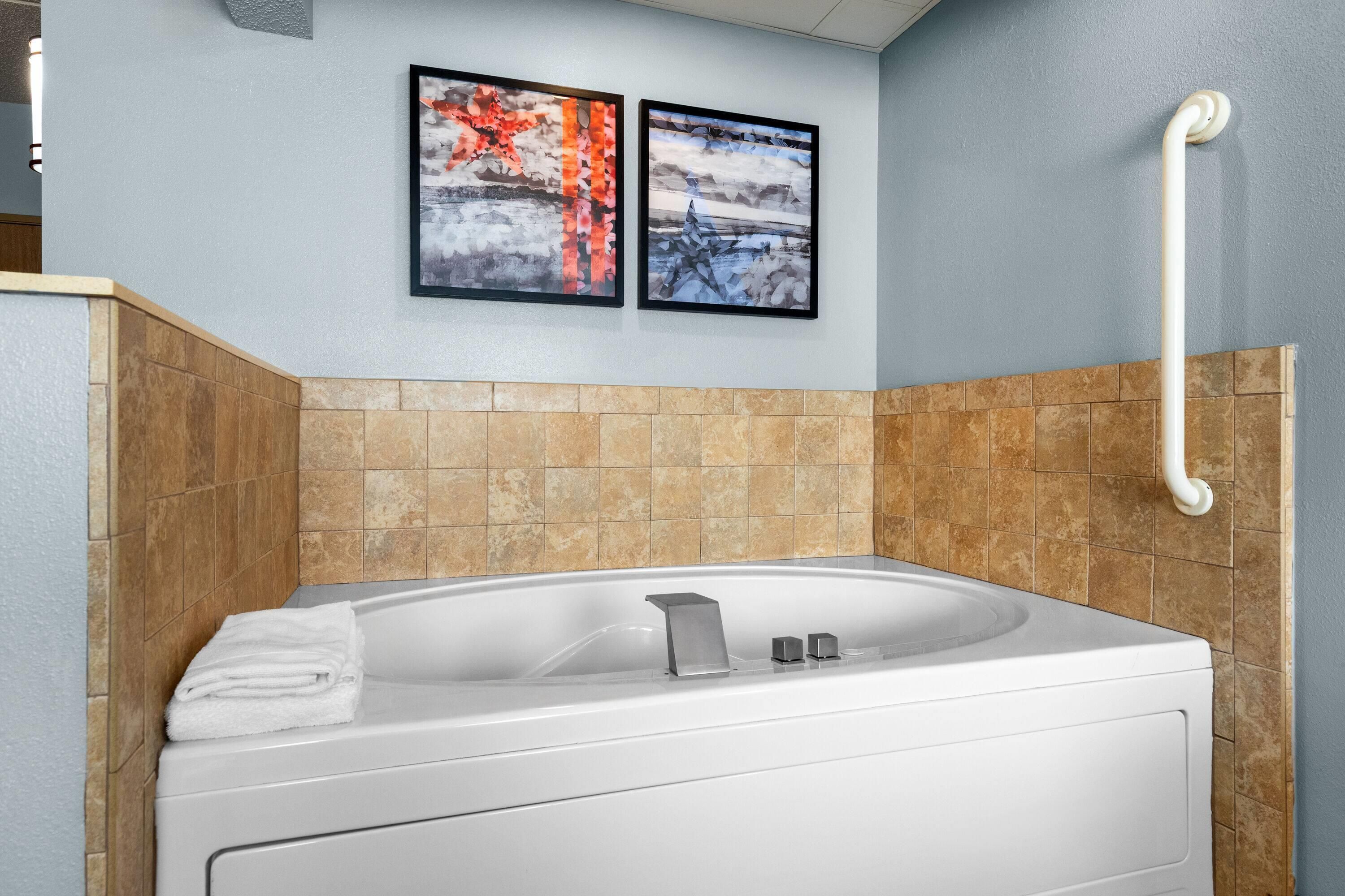 A modern bathroom with a white bathtub, a handrail, and two framed artworks on the wall.