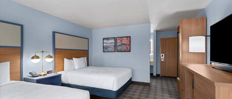 A hotel room with two beds, a desk, a TV, and a door leading to a bathroom.