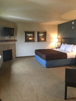 Habitación de hotel con cama, televisor montado en la pared, dos cuadros enmarcados, lámpara y una silla.