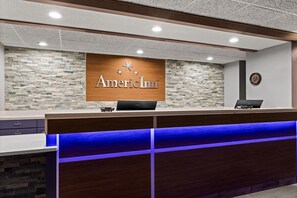Una recepción con un fondo de pared de piedra, un letrero de madera con el nombre 'AmerInn' y un reloj en la pared.