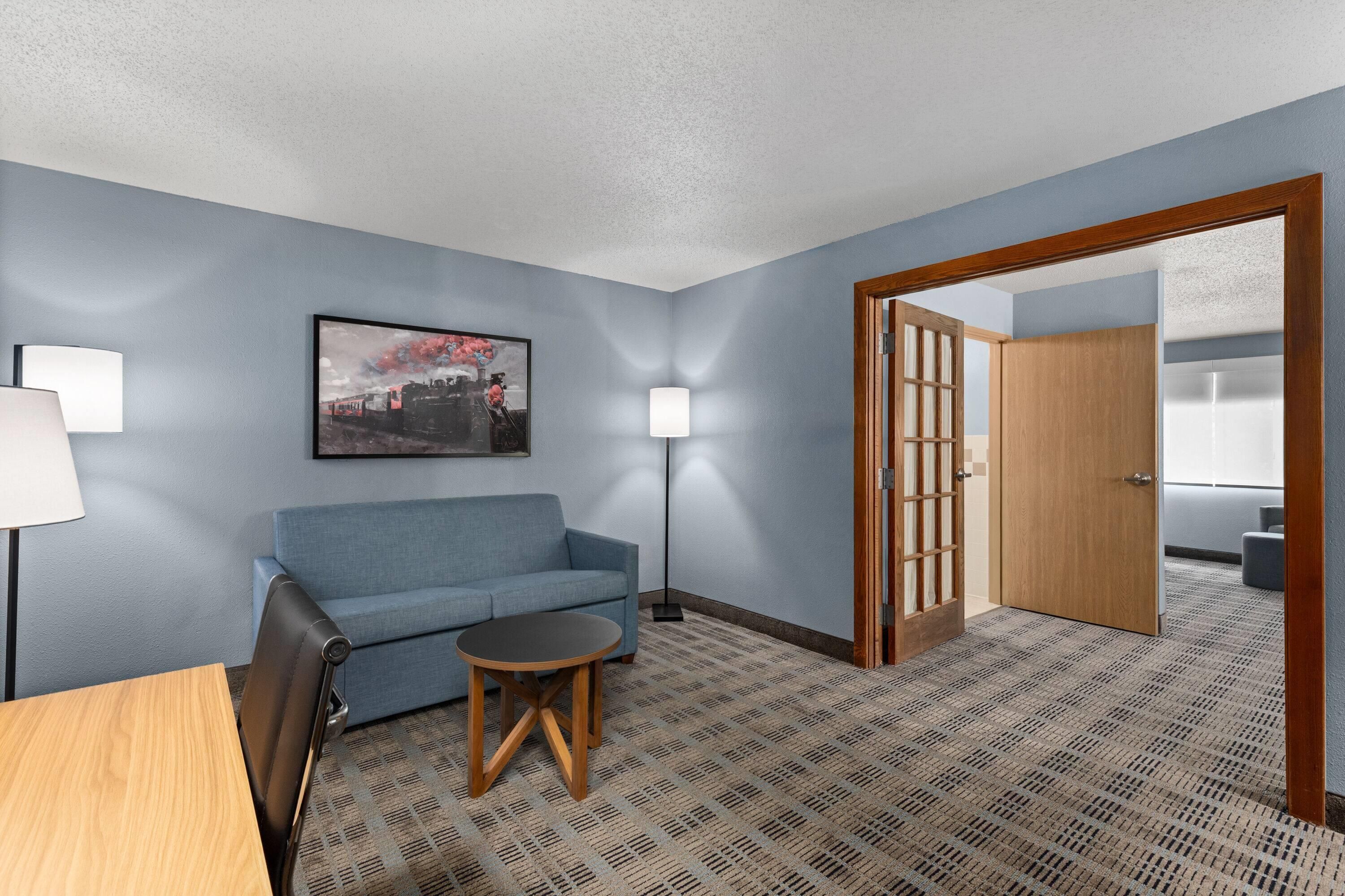 Ein Hotelzimmer mit einem blauen Sofa, einem kleinen runden Tisch, einer Lampe und einem Bild an der Wand.