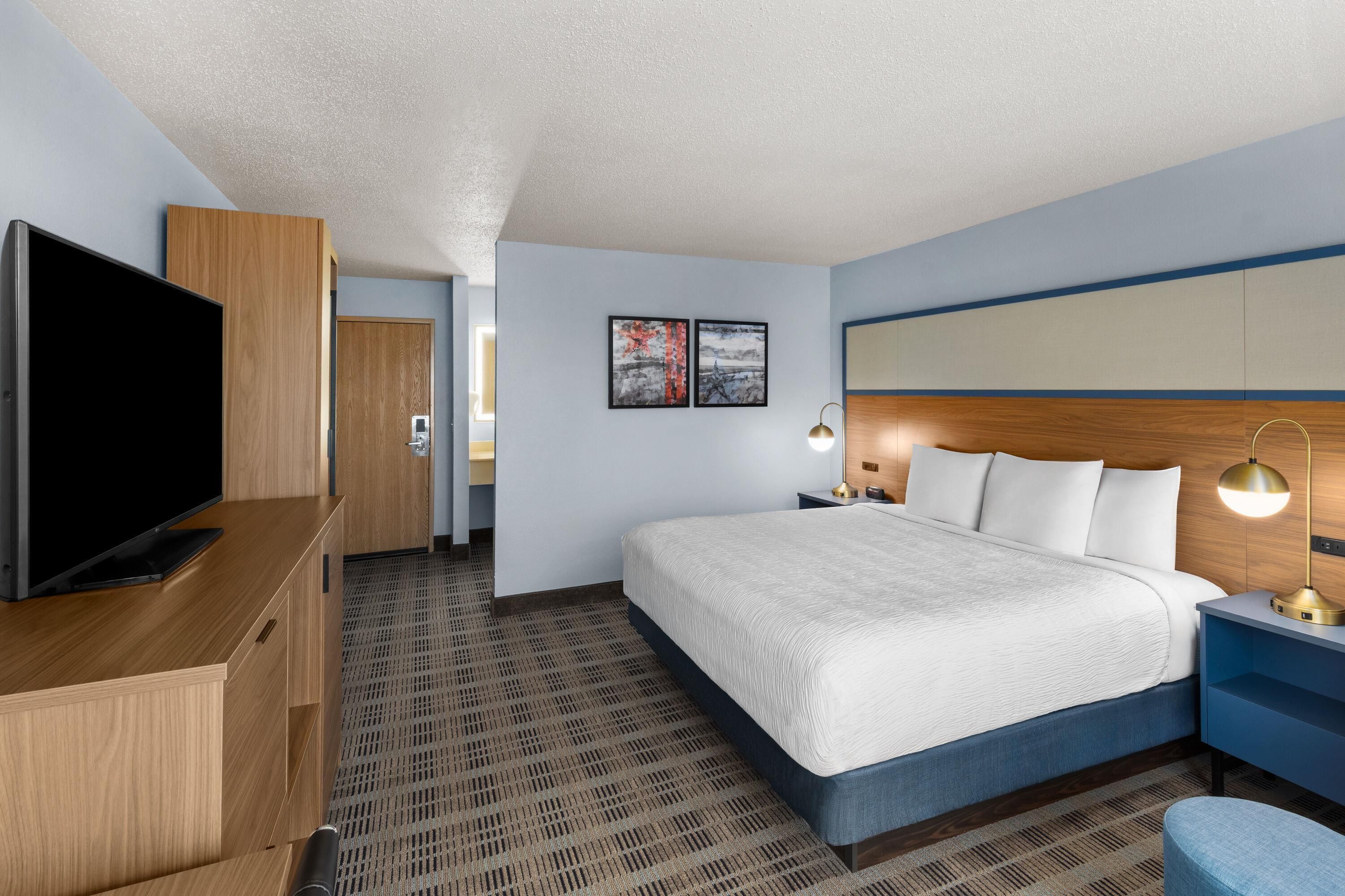 Una habitación de hotel con cama, televisor, escritorio y mesita de noche.