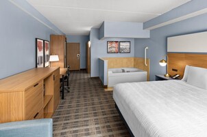A hotel room with a bed, a desk, a chair, a bathroom with a bathtub, and a shower.
