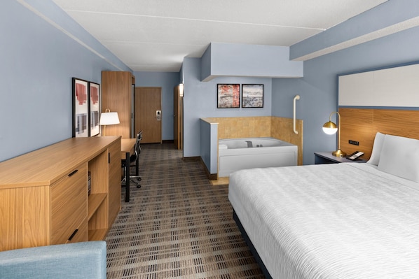 A hotel room with a bed, a desk, a chair, a bathroom with a bathtub, and a shower.