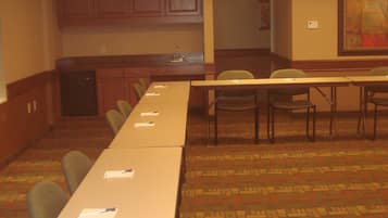 A conference room with a long table, chairs, a kitchenette, and an exit sign.