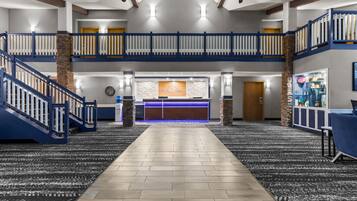 Eine Hotellobby mit einer zentralen Rezeption, einer Treppe und einer hohen Decke mit Ventilatoren.