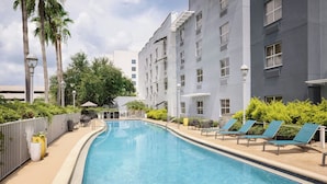 A swimming pool with lounge chairs, a fence, and a building with multiple windows.