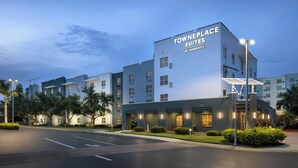 A modern hotel building with the name "Townplace Suites" by Marriott. It features multiple floors, a flat roof, and is surrounded by well-maintained landscaping.