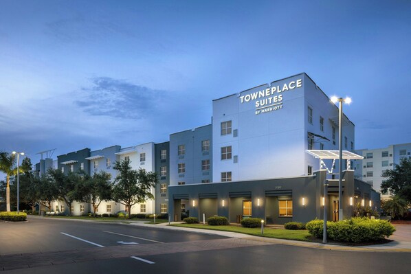 A modern hotel building with the name "Townplace Suites" by Marriott. It features multiple floors, a flat roof, and is surrounded by well-maintained landscaping.