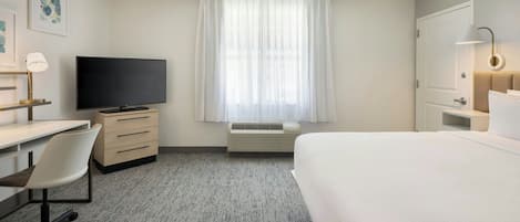 Ein Hotelzimmer mit Bett, Schreibtisch mit Stuhl, Fernseher und einem Fenster mit Vorhängen.