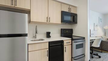 A modern kitchen with light wood cabinets, a stainless steel refrigerator, a black microwave, a coffee maker, and a dishwasher.