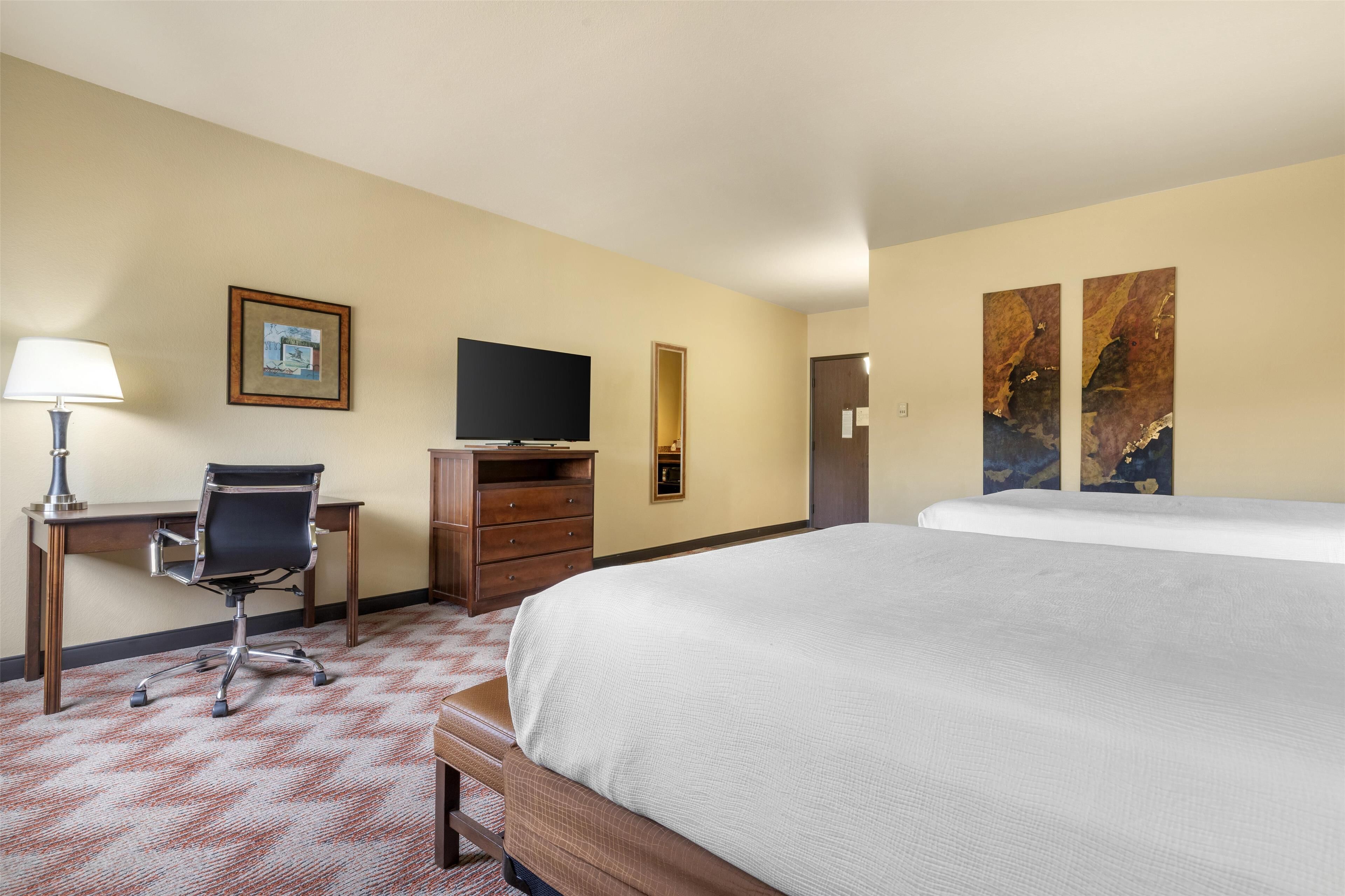 A hotel room with a bed, desk, chair, television, dresser, and artwork on the walls.