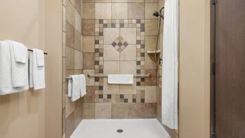 Ducha a nivel con suelo y paredes de azulejos, barra de apoyo y toallero con toallas.