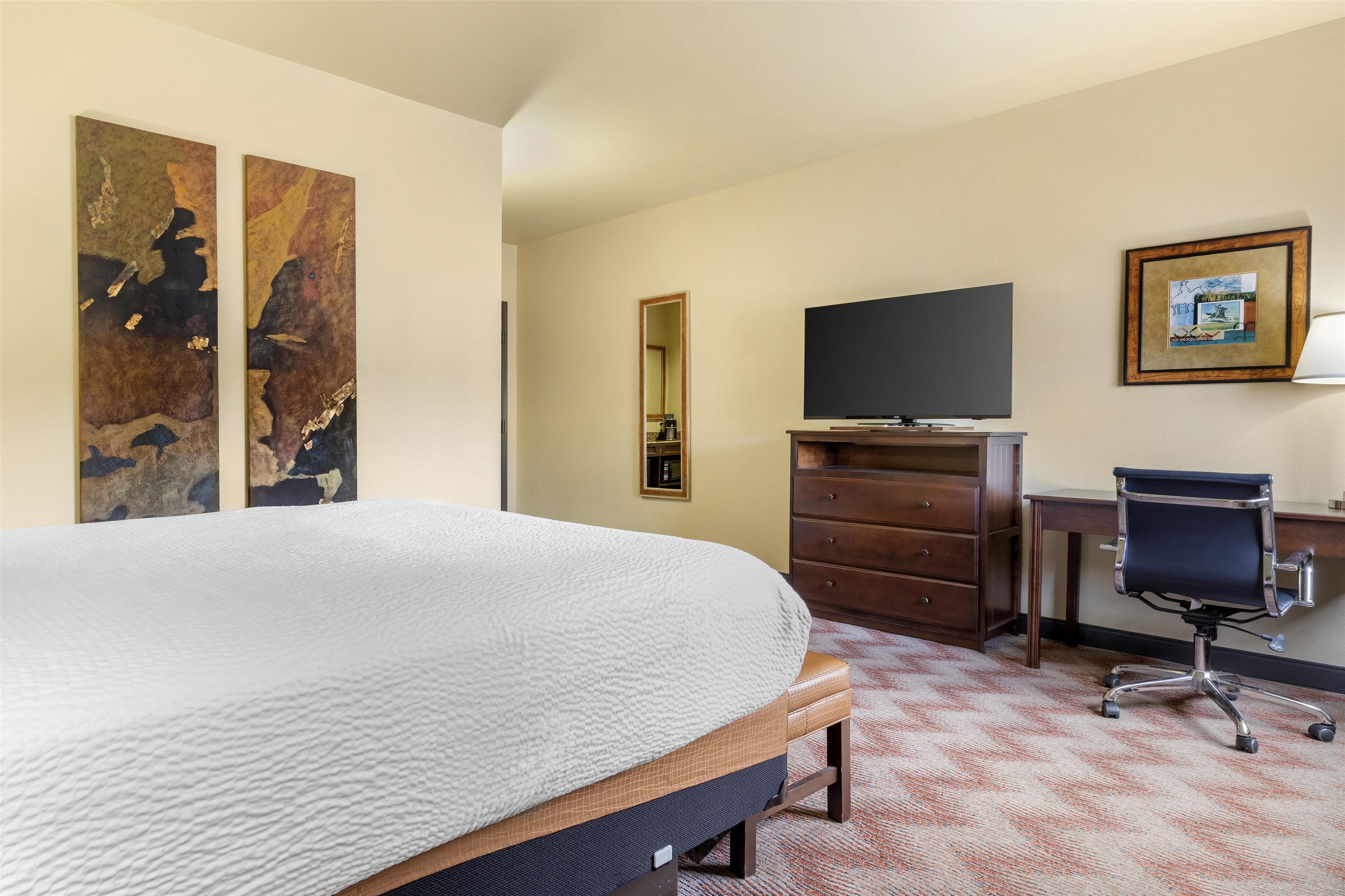 A hotel room with a large bed, a desk with a chair, a television, and artwork on the walls.
