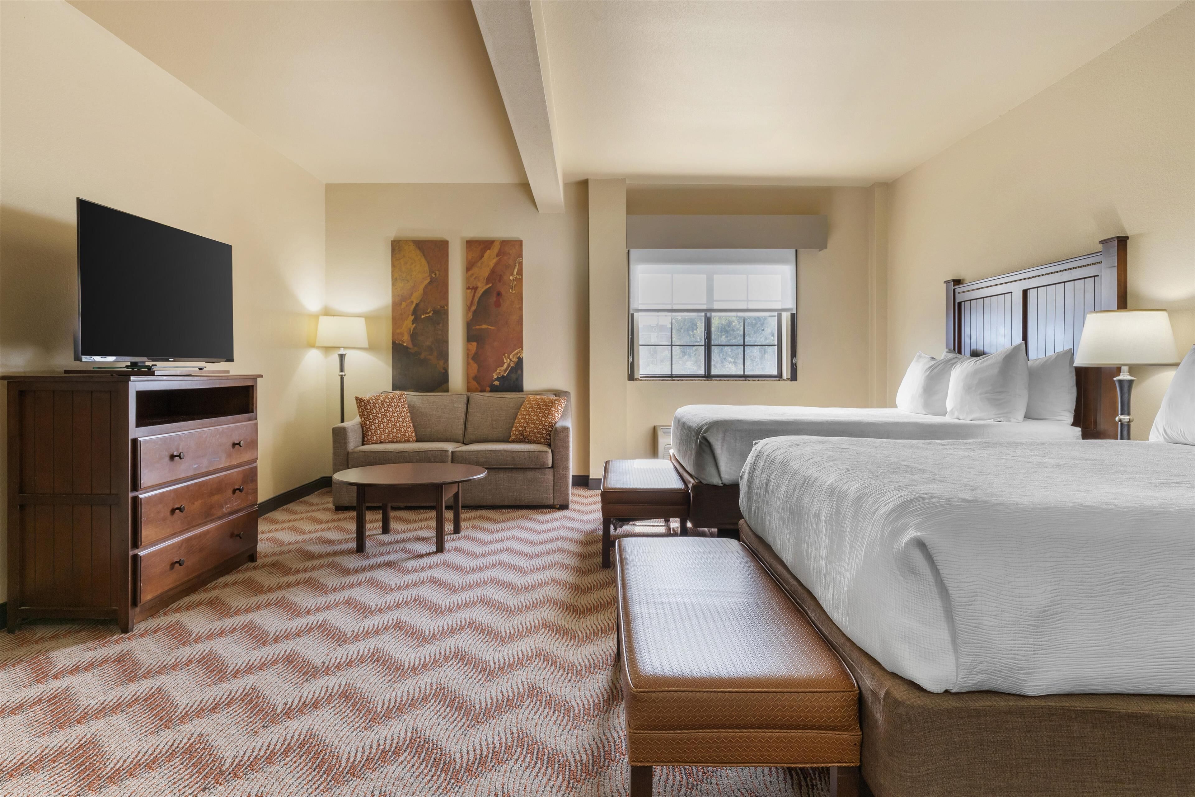 A hotel room with a large bed, a sofa, a TV, a desk, and a window.