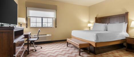 A hotel room with a bed, bedside tables, a desk with a chair, a TV, and a window with blinds.
