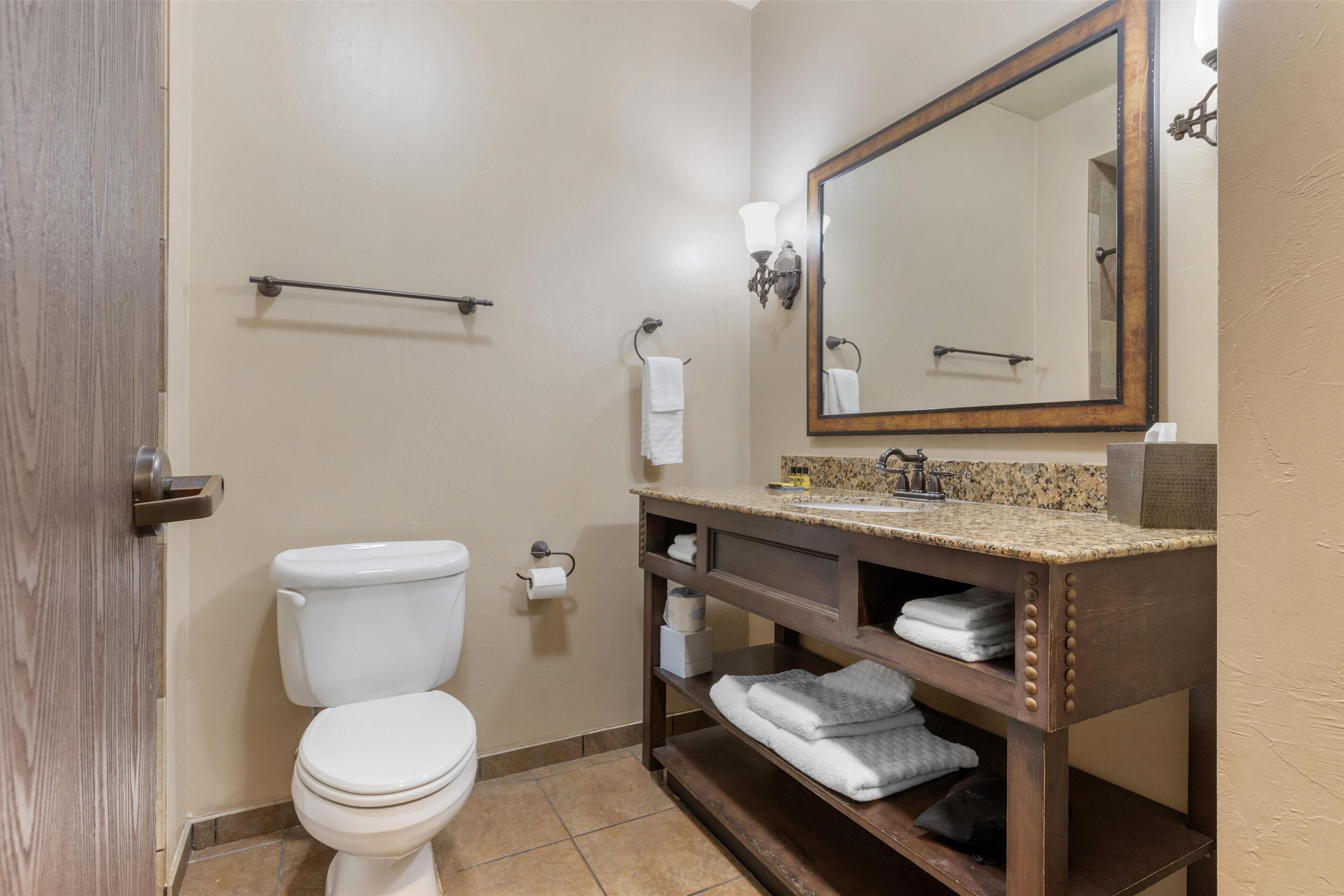 A bathroom with a toilet, sink, mirror, towel rack, and shelves.
