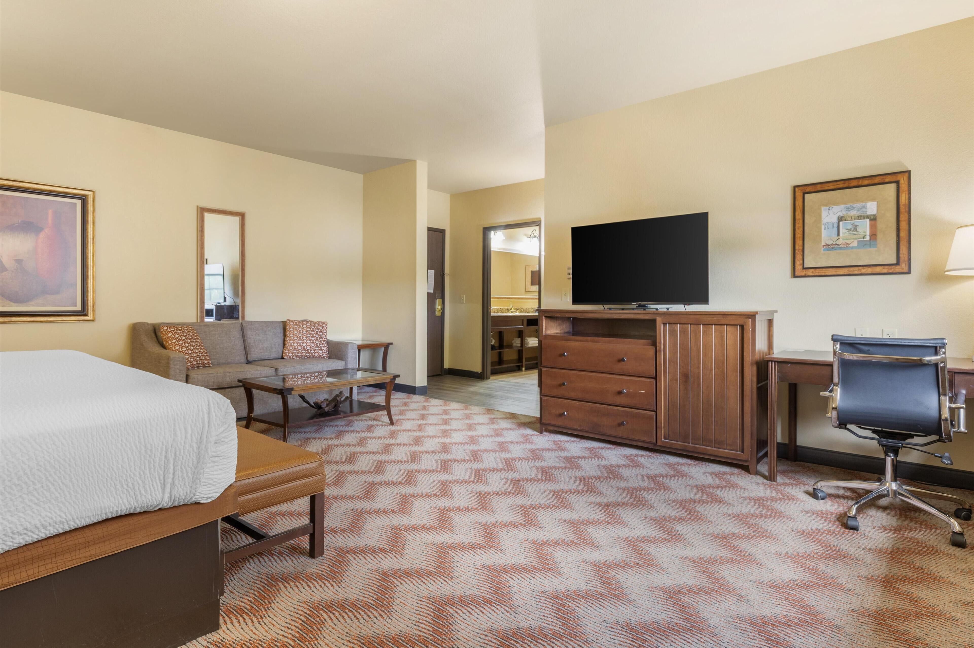 A hotel room with a bed, a sofa, a desk, a chair, a television, and a dresser.