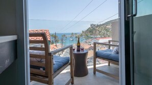 A balcony with two wooden chairs and a small round table, overlooking a coastal area with buildings and a clear sky. - Aurora Hotel (Avalon)