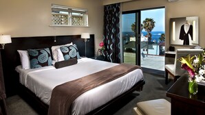 A hotel room with a large bed, a desk, a chair, a mirror, and a view of the ocean. - Aurora Hotel (Avalon)