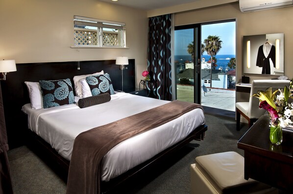 A hotel room with a large bed, a desk, a chair, a mirror, and a view of the ocean. - Aurora Hotel (Avalon)