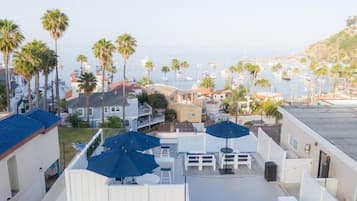 Une terrasse sur le toit, dotée de sièges extérieurs et de parasols, qui offre une vue sur une marina avec des bateaux et des palmiers.