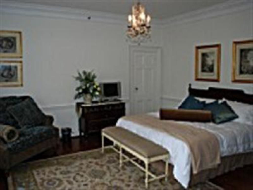 A bedroom with a bed, bedside table, bench, dresser, and a chandelier.