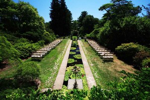 Jardim formal com fonte central, disposição simétrica de assentos e vegetação exuberante.