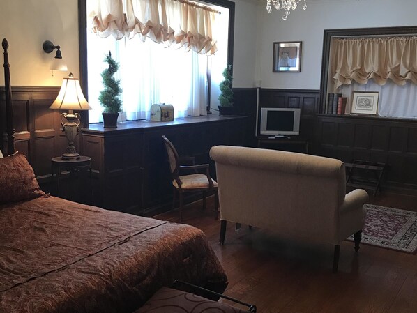 A hotel room with a bed, a desk with a computer, a chair, a lamp, and a window with curtains. - The Castle at Skylands Manor (Ringwood)
