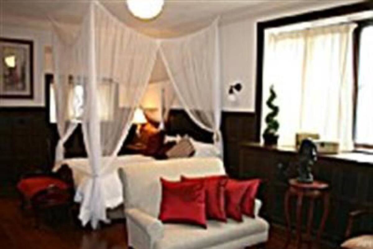 Une pièce avec un canapé blanc, des coussins rouges, un lit à baldaquin blanc et un plancher en bois.