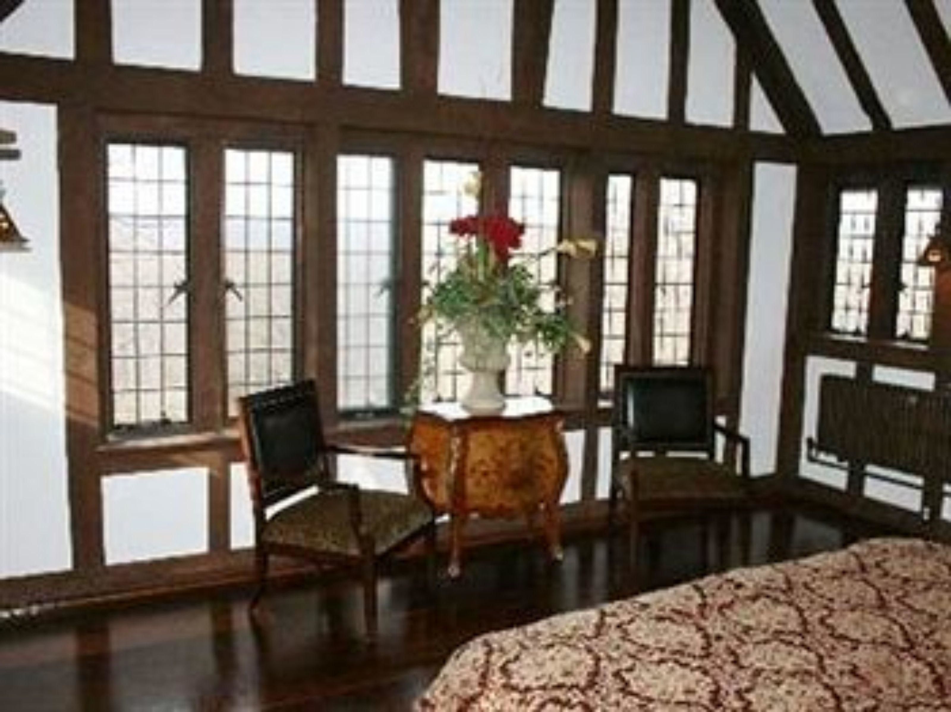 Quarto com grandes janelas, uma cama e duas cadeiras.