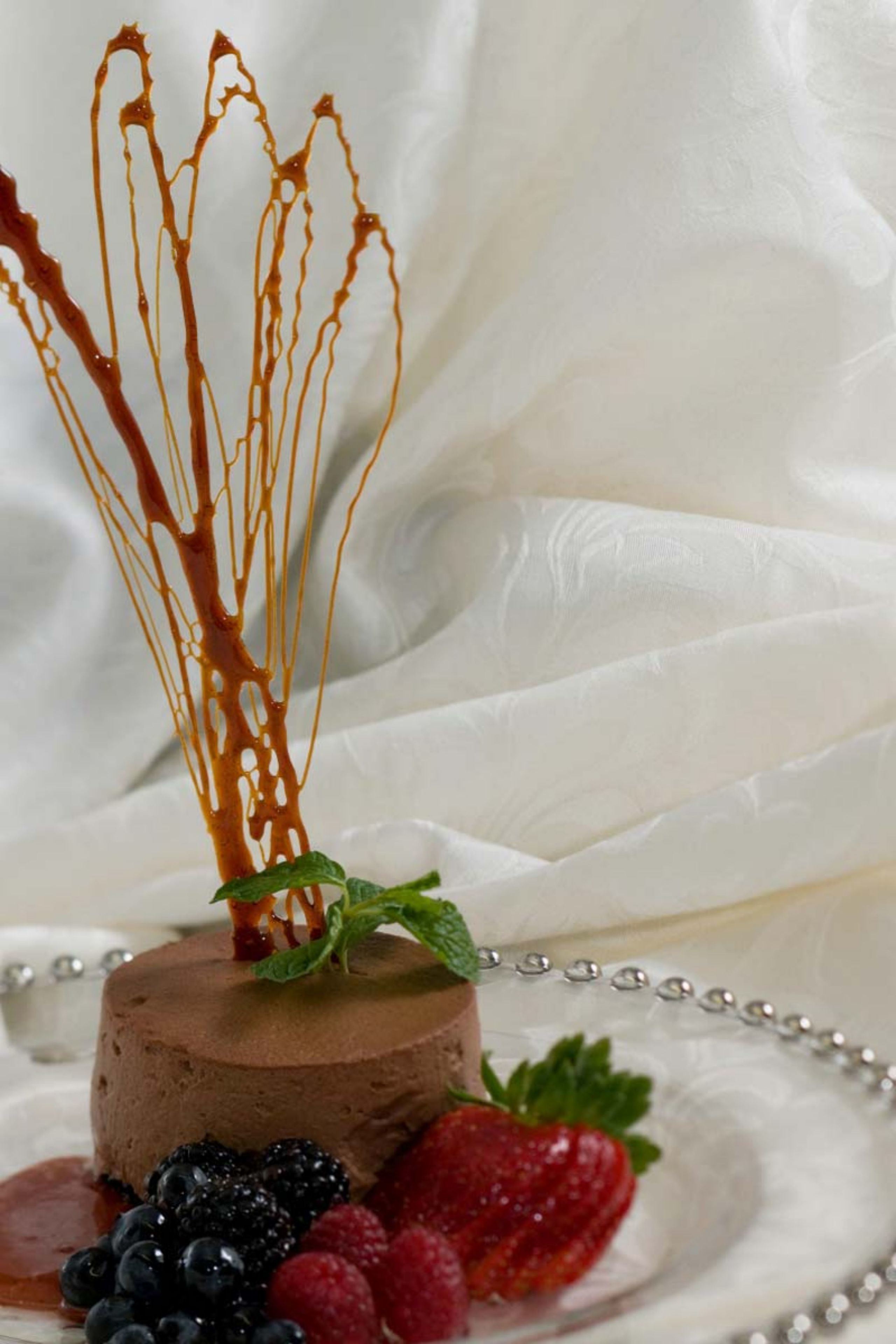 En dessert med chokolademousse, jordbær, blåbær, hindbær og et mynteblad, pyntet med chokoladesauce.