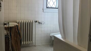 A bathroom with white tiled walls, a radiator, a toilet, and a window with a diamond pattern.