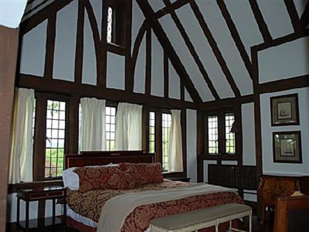 A traditional room with exposed wooden beams, a large bed with a patterned bedspread, and multiple windows with curtains.