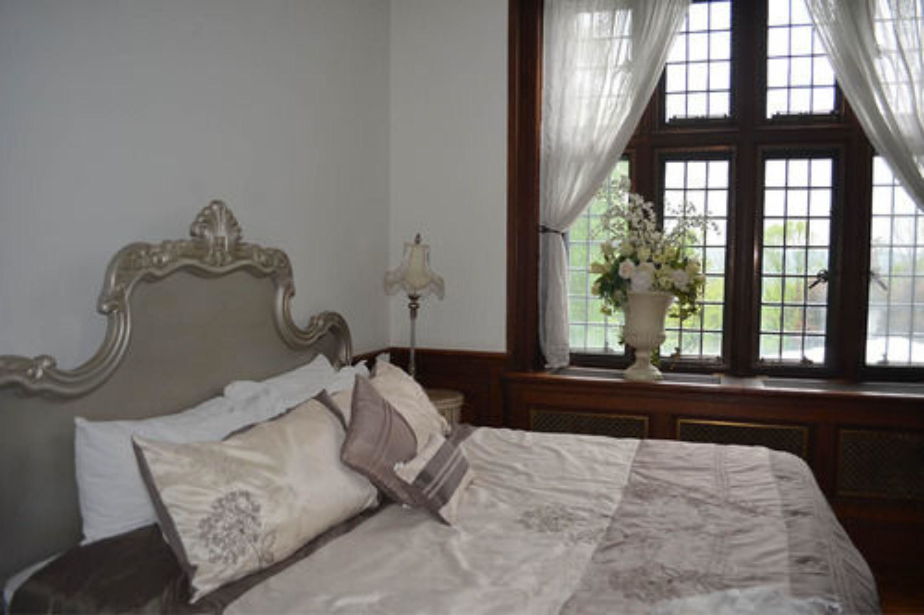 A bedroom with a large bed, a nightstand with a lamp, and a window with curtains.