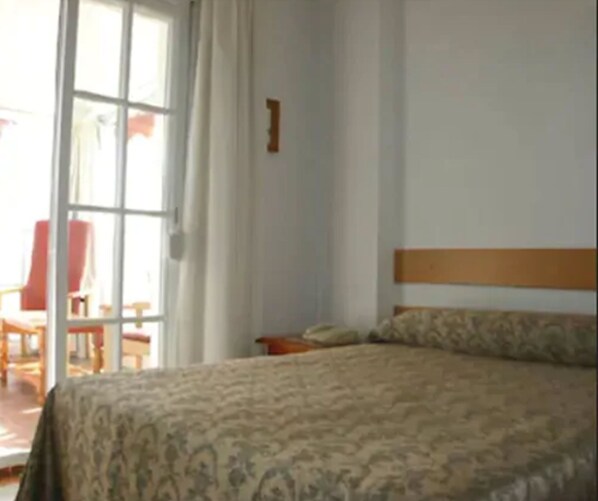 A bedroom with a bed, a chair, and a window.
