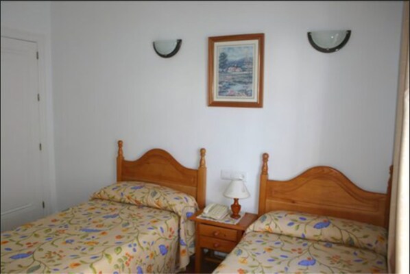 Un dormitorio con dos camas individuales, una mesita de noche con lámpara y un cuadro en la pared.