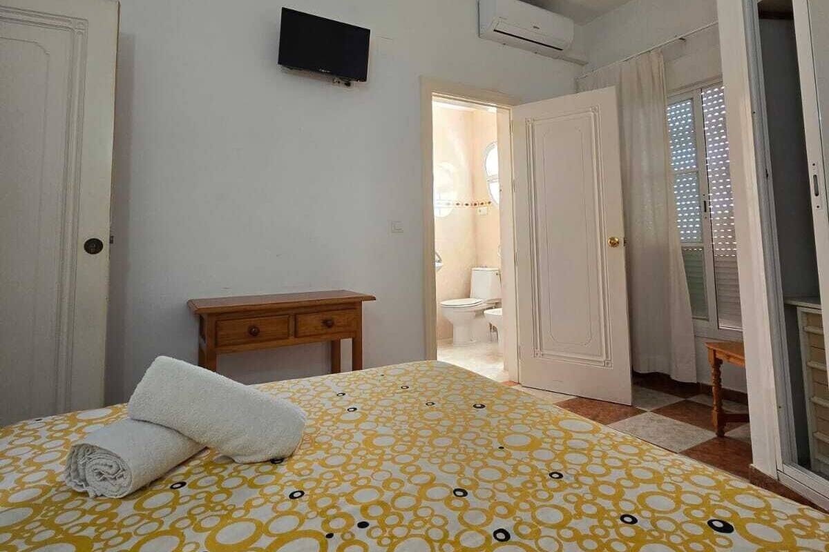 Une chambre à coucher comprenant un lit, une table de chevet, un téléviseur, un appareil de climatisation et une salle de bain visible à travers une porte ouverte.