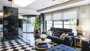 A modern lobby with a checkered floor, black leather sofas, a round coffee table with a vase of flowers, and a large window offering a view of the outdoors. - Salles Hotel Aeroport de Girona (Riudellots de la Selva)