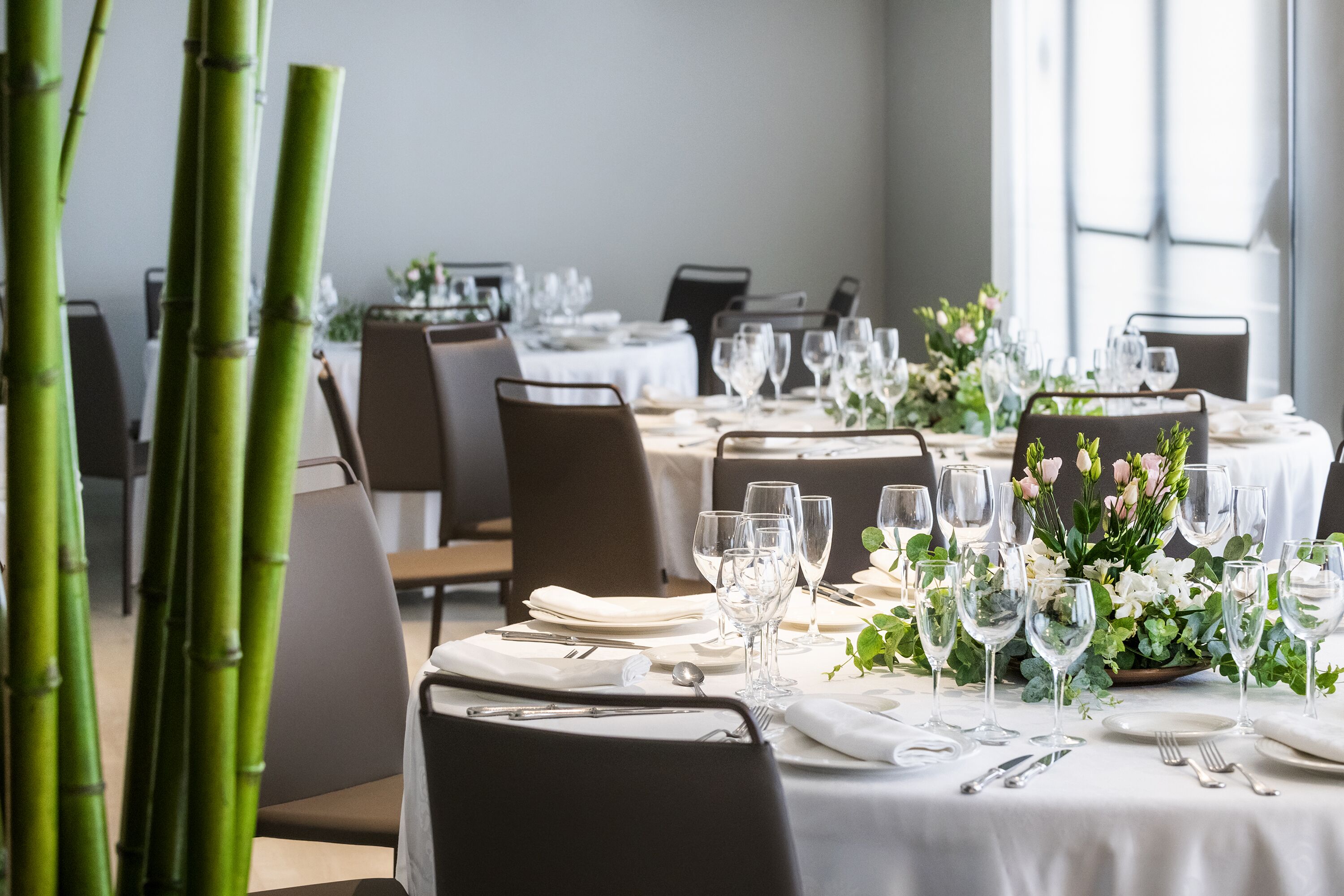Un espace repas avec des tables dressées pour le repas, agrémenté de nappes blanches, de verres et de compositions florales.