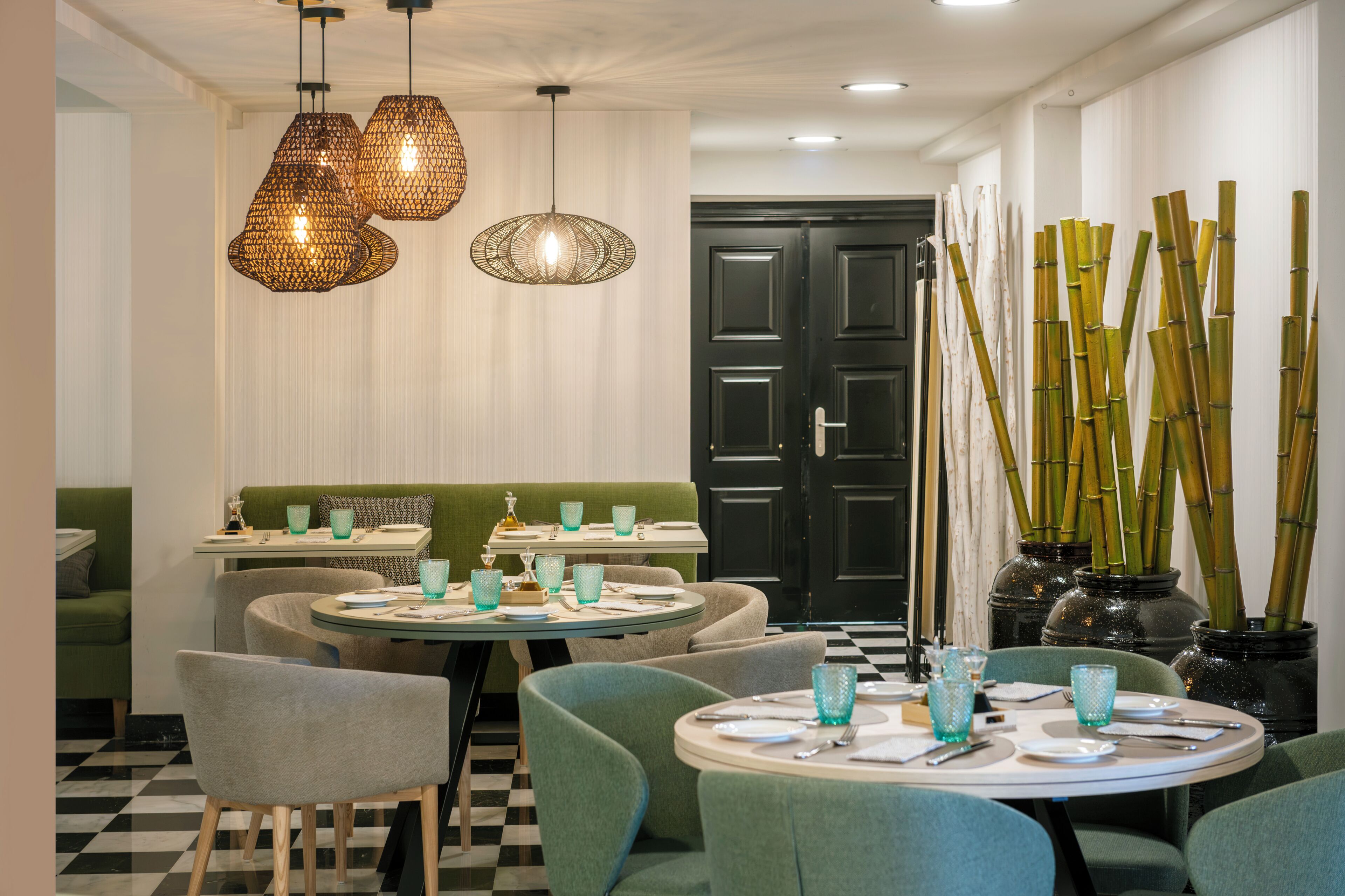 L’intérieur d’un restaurant avec des tables rondes, des chaises recouvertes d’un tissu vert et des lampes suspendues.