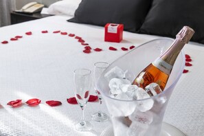 A bed with rose petals arranged in a heart shape, a bottle of champagne, and two glasses on a white tablecloth. - Salles Hotel Aeroport de Girona (Riudellots de la Selva)
