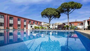 A swimming pool with lounge chairs and umbrellas, surrounded by buildings with red and white facades. - Salles Hotel Aeroport de Girona (Riudellots de la Selva)