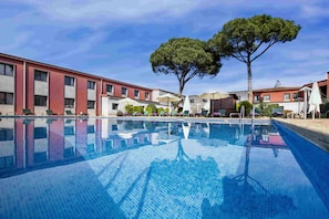 A swimming pool with lounge chairs and umbrellas, surrounded by buildings with red and white facades.