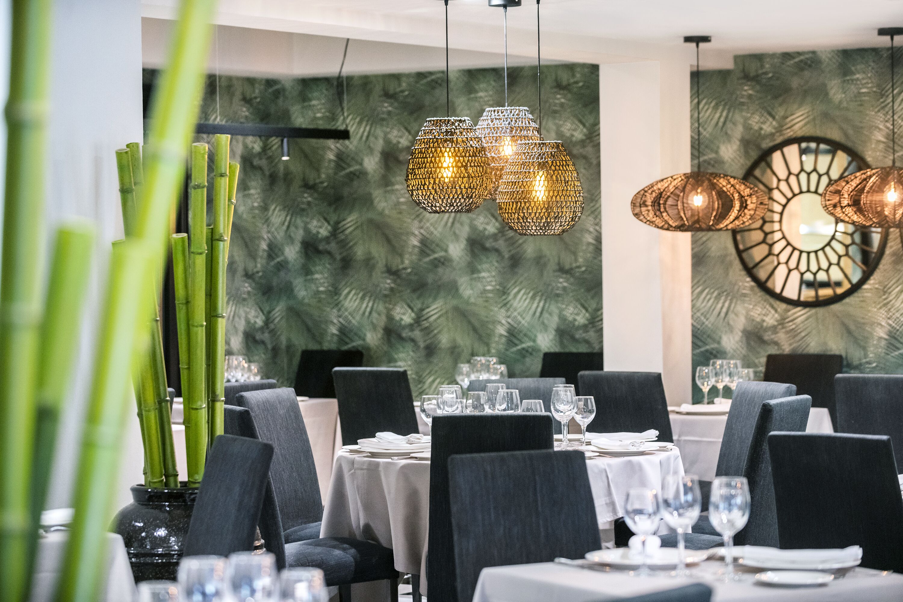Un restaurant avec des tables dressées pour le service, des plantes en bambou et un éclairage décoratif.